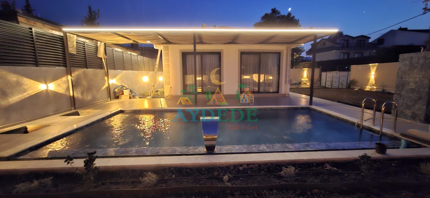 Seydikemer Alaçat mevkiinde yer alan tek katlı lüks Villa Morgan'ın akşam ışıklandırmalı özel yüzme havuzu ve dış cephe görünümü.